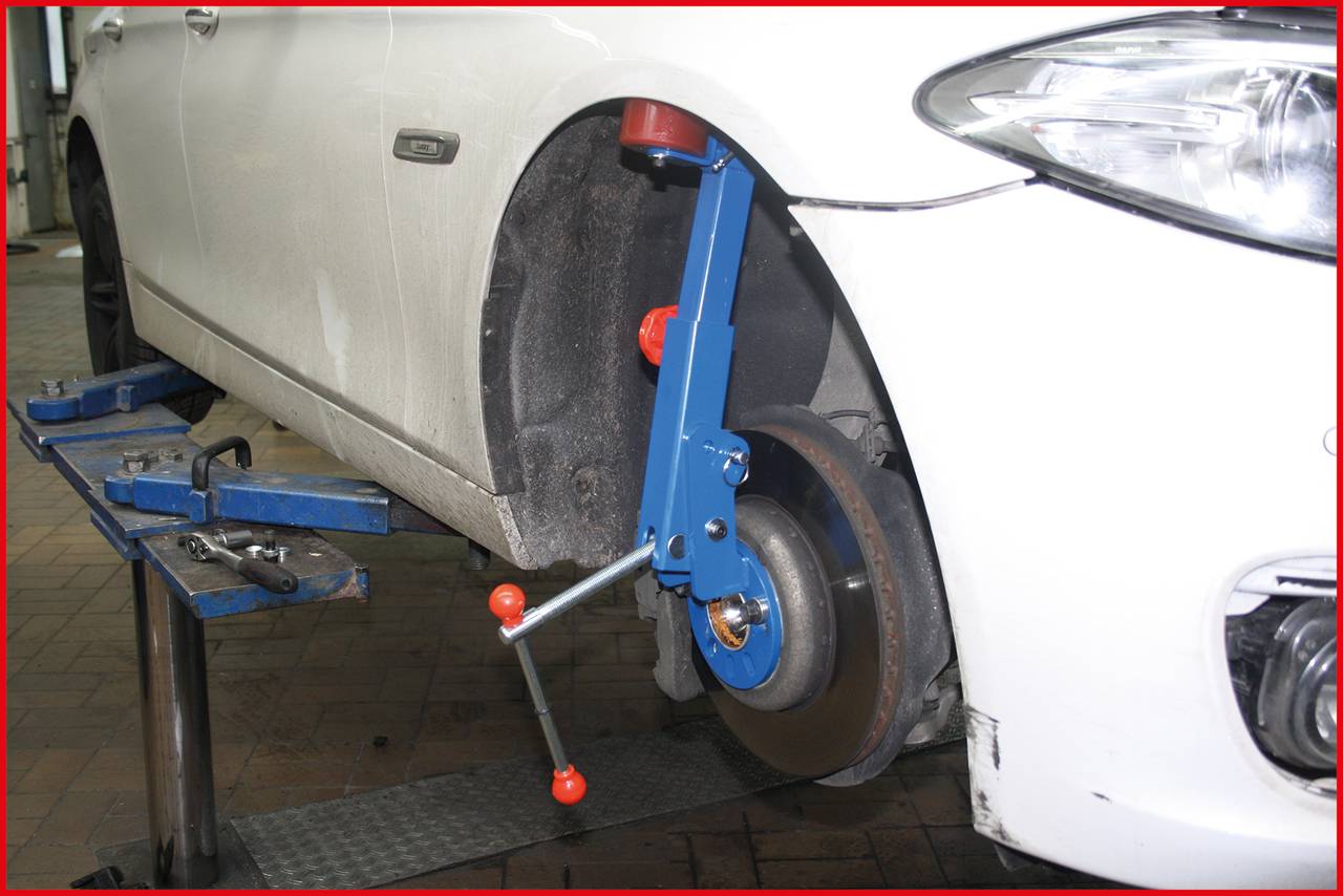 Ein weißes Auto in einer Werkstatt mit einem Rad, das mit einem blauen Gerät für eine Achsvermessung ausgestattet ist.
