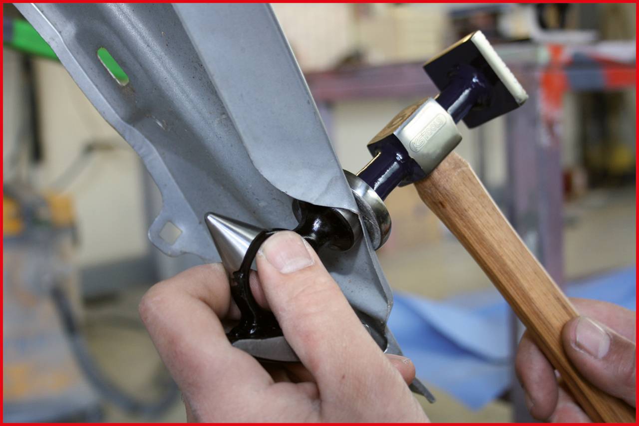 Nahaufnahme von Händen, die Metall mit einem Hammer und einem Formwerkzeug bearbeiten, um es in die gewünschte Form zu biegen.