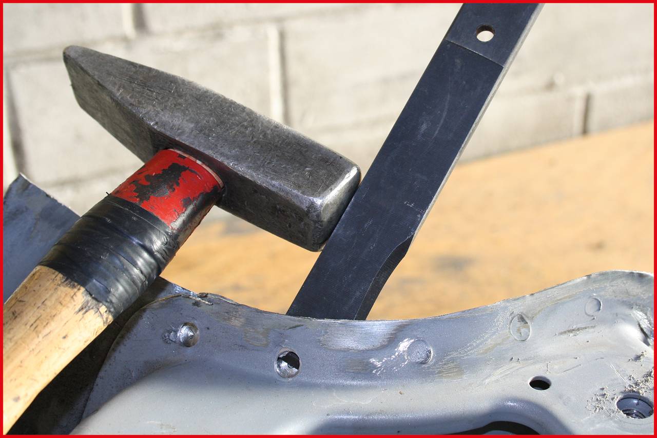 Hammer und Meißel auf einem Metallobjekt in einer Werkstattumgebung. Das Bild zeigt handwerkliche Werkzeuge in Benutzung.