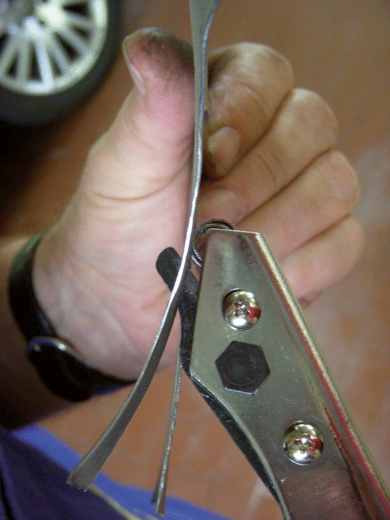 Eine Hand schneidet mit einem Werkzeug ein Stück Metallband. Der Hintergrund ist verschwommen.