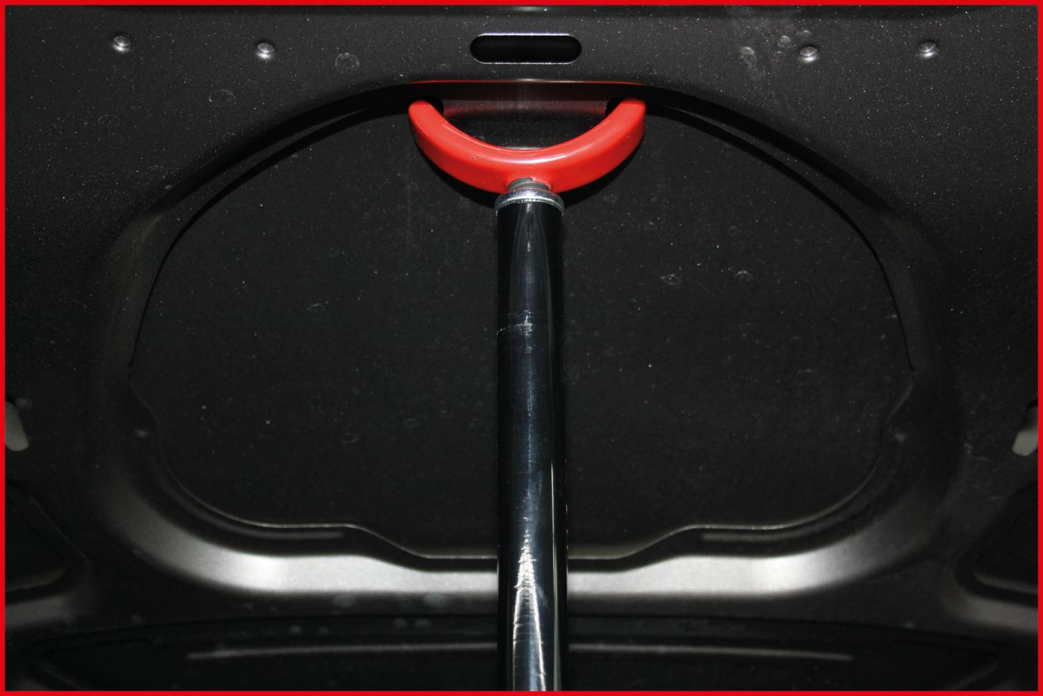 Auto-Motorhaube mit Stützstange in der Mitte, versehen mit rotem Griff zum Anheben oder Stabilisieren der geöffneten Klappe.