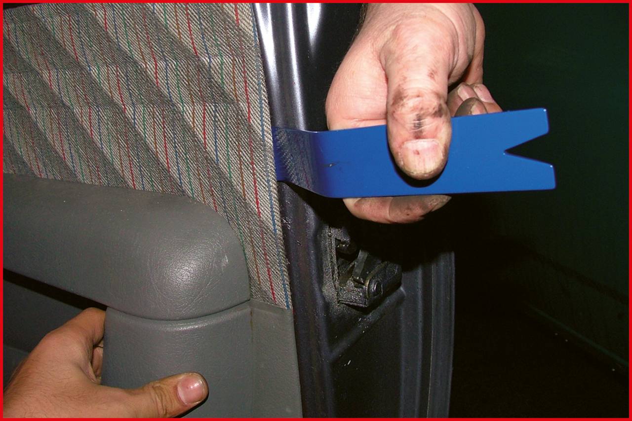Eine Person entfernt die Verkleidung eines Autotürrahmens mit einem blauen Plastikwerkzeug, um an die inneren Teile zu gelangen.