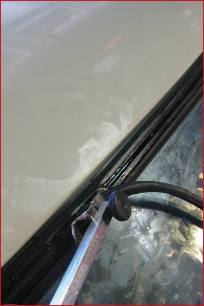 Ein Metallwerkzeug hebt die Gummidichtung an einer Autotür an. Im Hintergrund ist ein Teil der Autotür sichtbar.