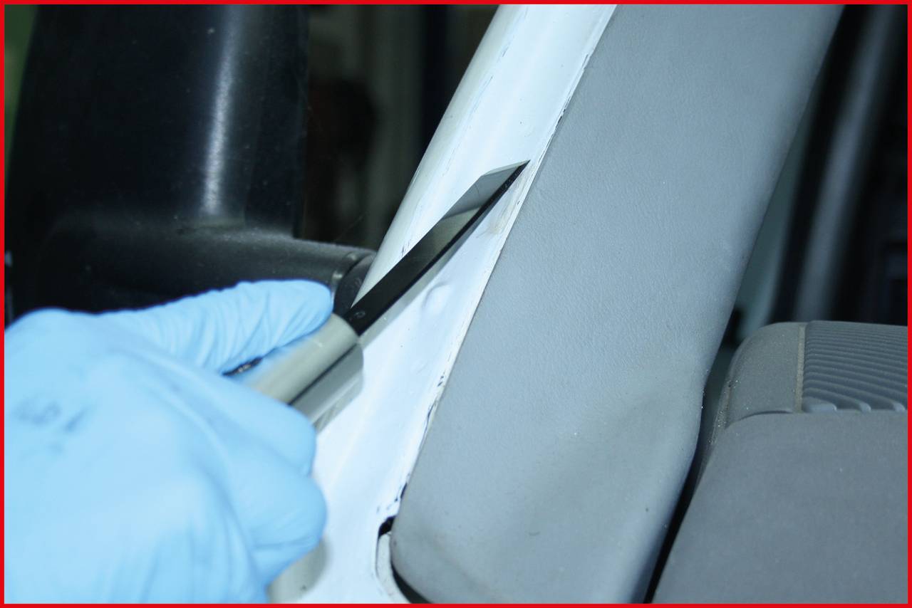 Eine Person in blauen Handschuhen hält ein Messer und schneidet vorsichtig an einem weißen Autoteil nahe dem Sitz entlang.