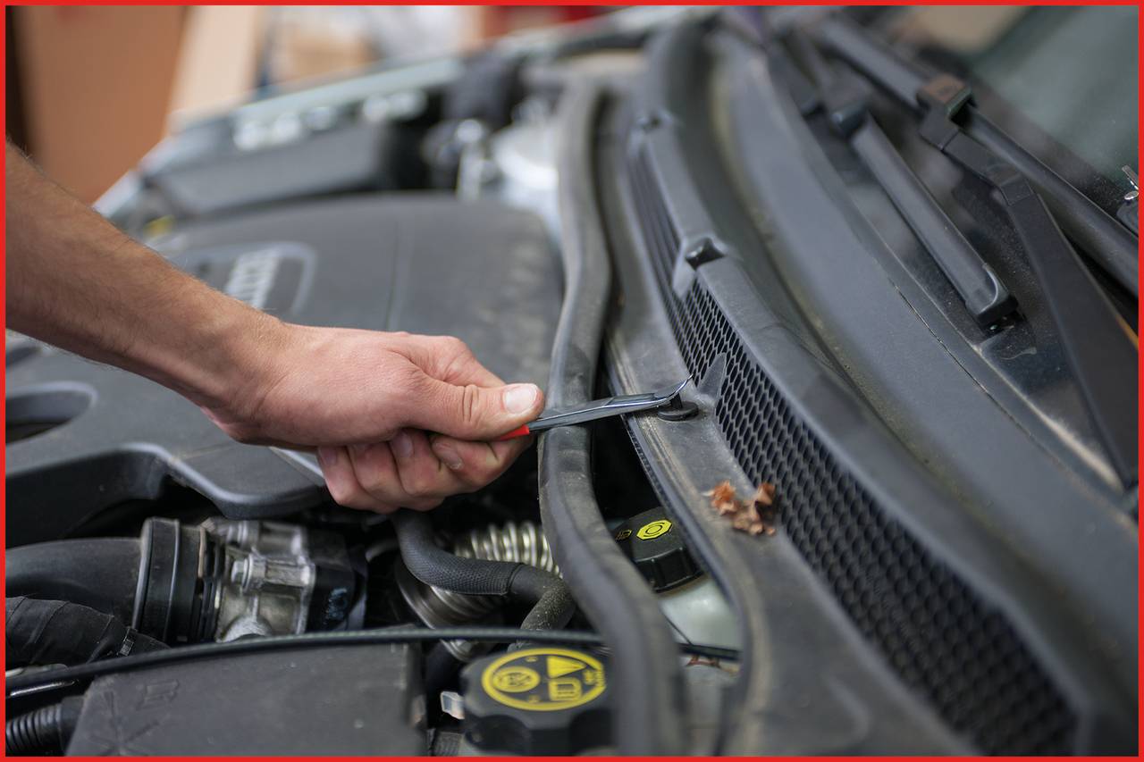 Eine Hand repariert den Motorraum eines Autos mit einem Schraubenschlüssel. Der Fokus liegt auf der Motorwartung.