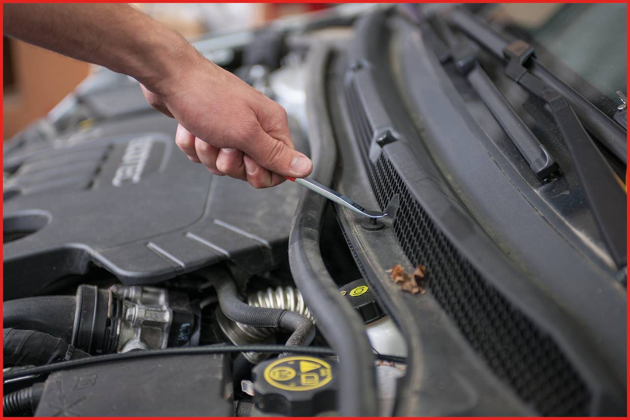 Person repariert Motorraum eines Autos mit Schraubendreher, Nahaufnahme von Hand und Motorraumdetails.