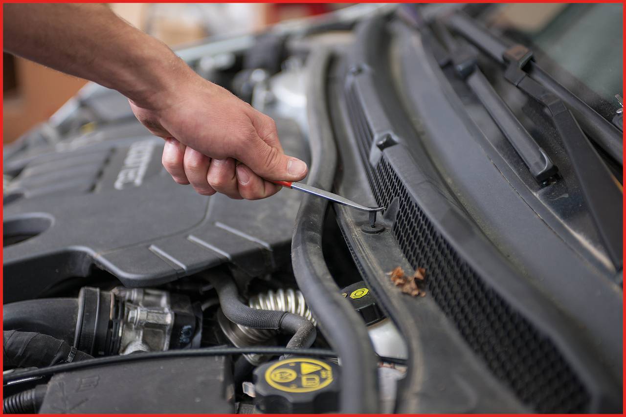 Eine Hand verwendet ein Schraubenzieher-Werkzeug, um an der Motorhaube eines Autos zu arbeiten.