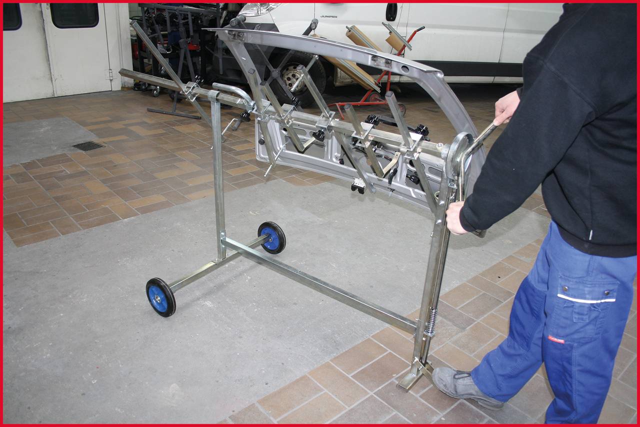 Eine Person bewegt einen metallischen Wagen mit Metallrahmen und blauen Rädern auf einer gepflasterten Fläche.