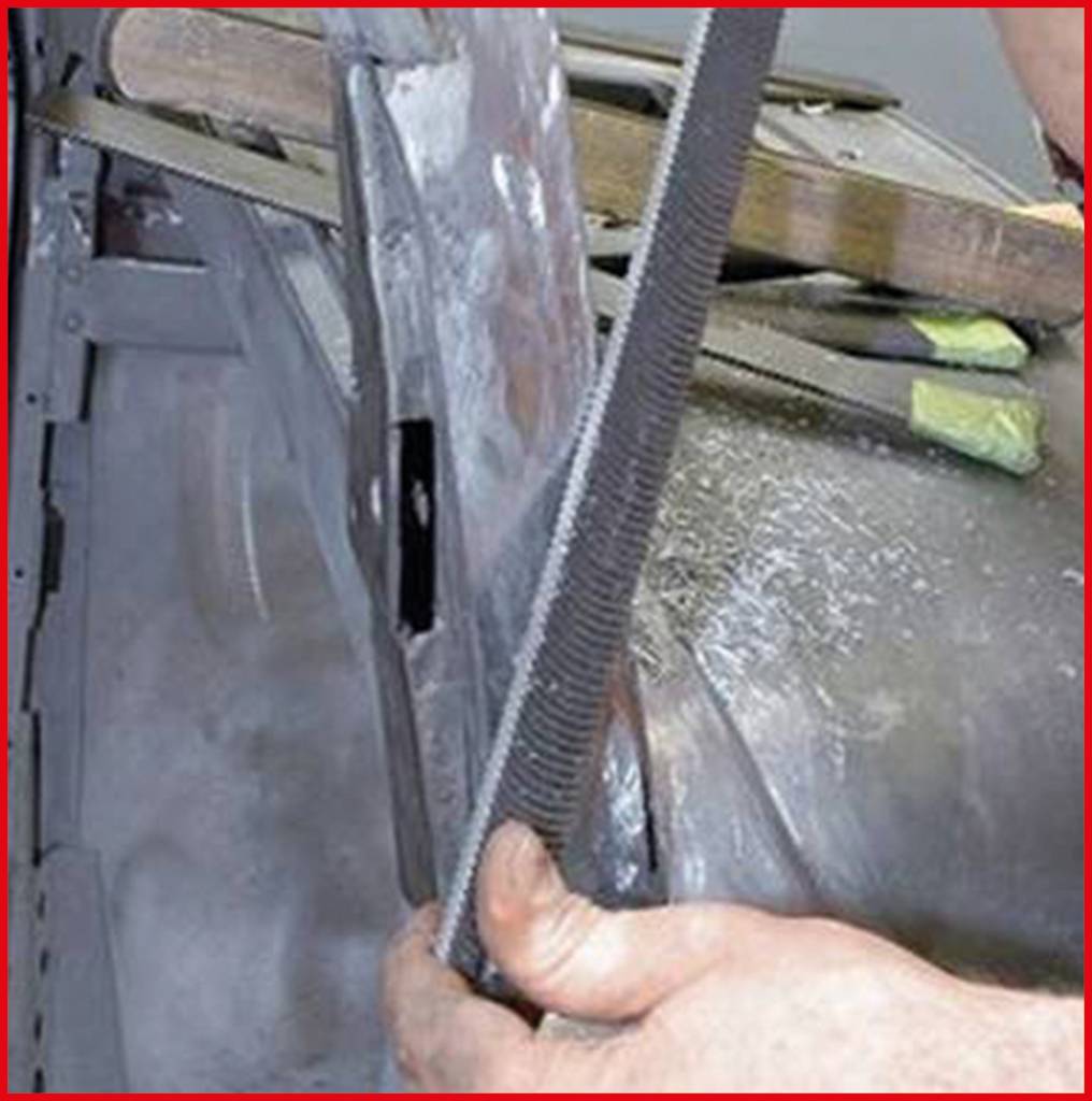 Hand mit Feile glättet eine Metalloberfläche. Im Hintergrund sind Teile einer Arbeitsfläche und Werkzeuge sichtbar.