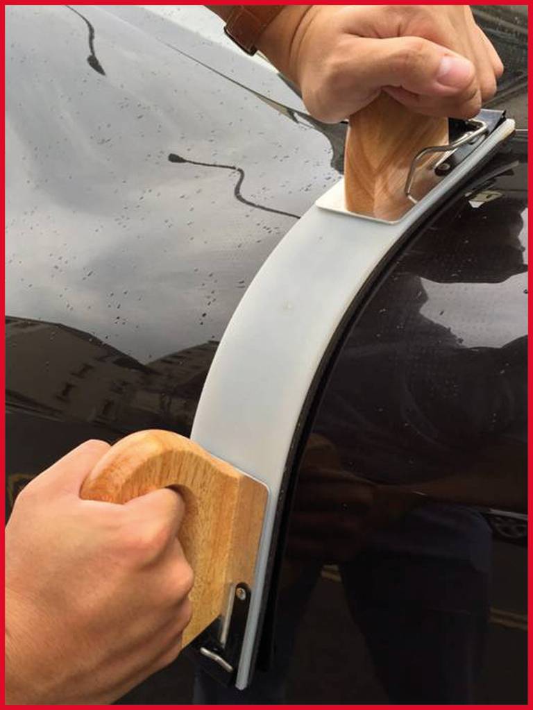 Zwei Hände halten Holzgriffe, die an einem großen Saugnapf befestigt sind, der auf der Oberfläche eines Autos angebracht ist.