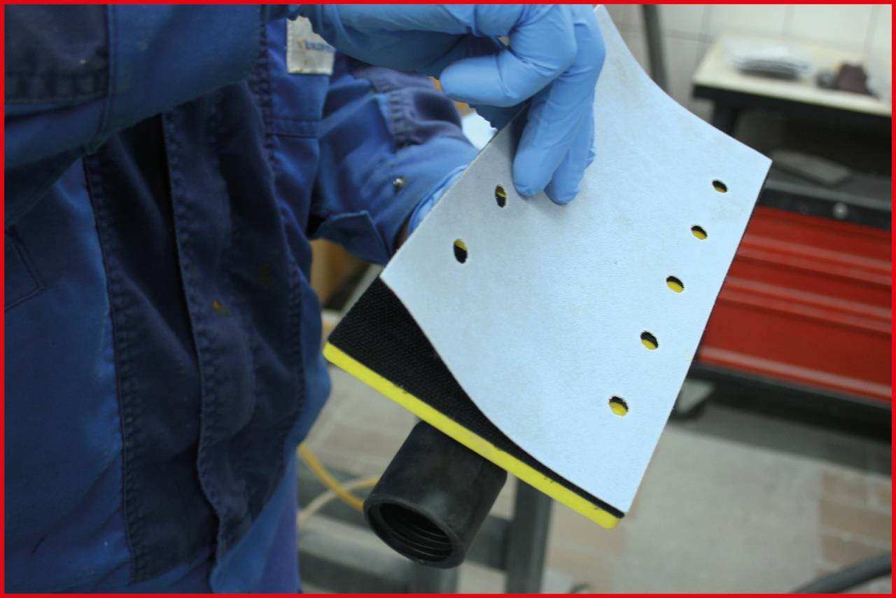 Eine Person in blauer Arbeitskleidung hält perforiertes Schleifpapier, bereit für den Einsatz im Handwerksbereich.