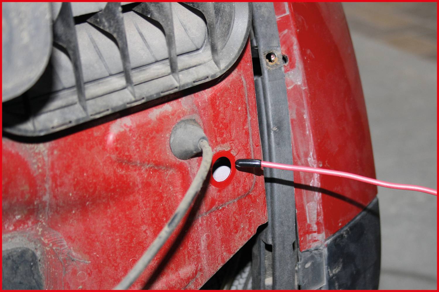 Ein Kabel wird durch ein Loch im Inneren eines roten Fahrzeugs gezogen. Der Bereich wirkt staubig und teilweise schmutzig.