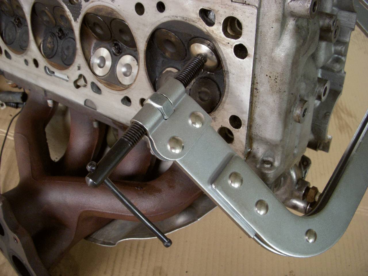 Metallzwinge hält Autozylinderkopfdichtung an Ort und Stelle. Der Motorblock zeigt Ventile und einen Krümmer. Mechanische Wartung.