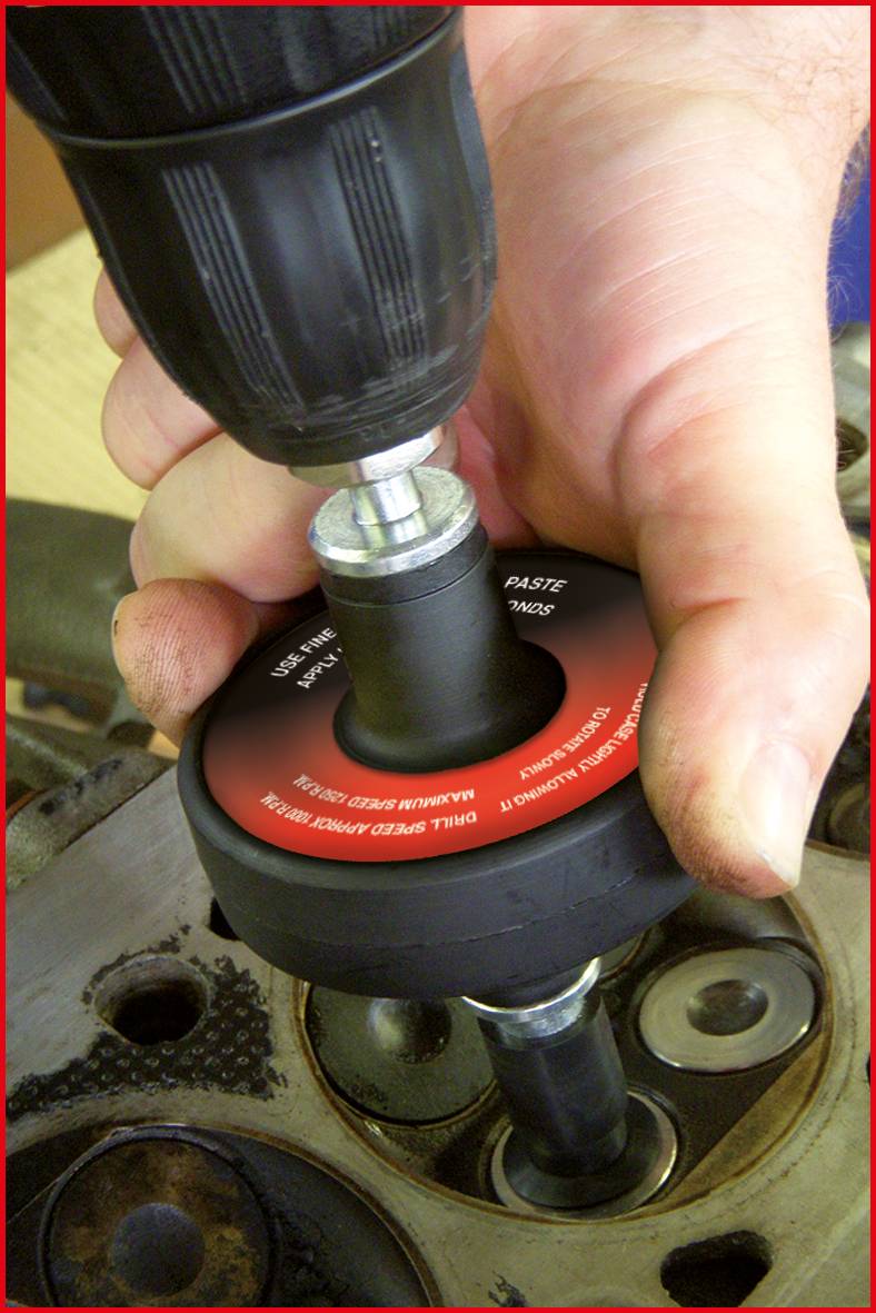 Nahaufnahme einer Hand, die mit einem Bohrer ein Ventilsitz-Werkzeug im Zylinderkopf einer Maschine anwendet.