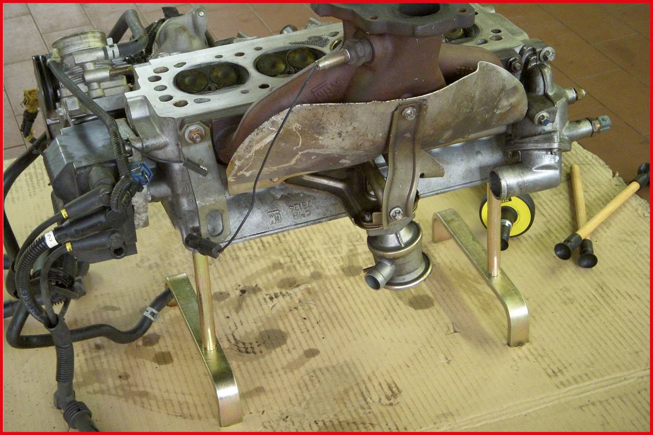 Motorblock auf Kartonunterlage mit verschiedenen Werkzeugen, darunter ein Messband und Hämmer. Der Motor ist teilweise demontiert.
