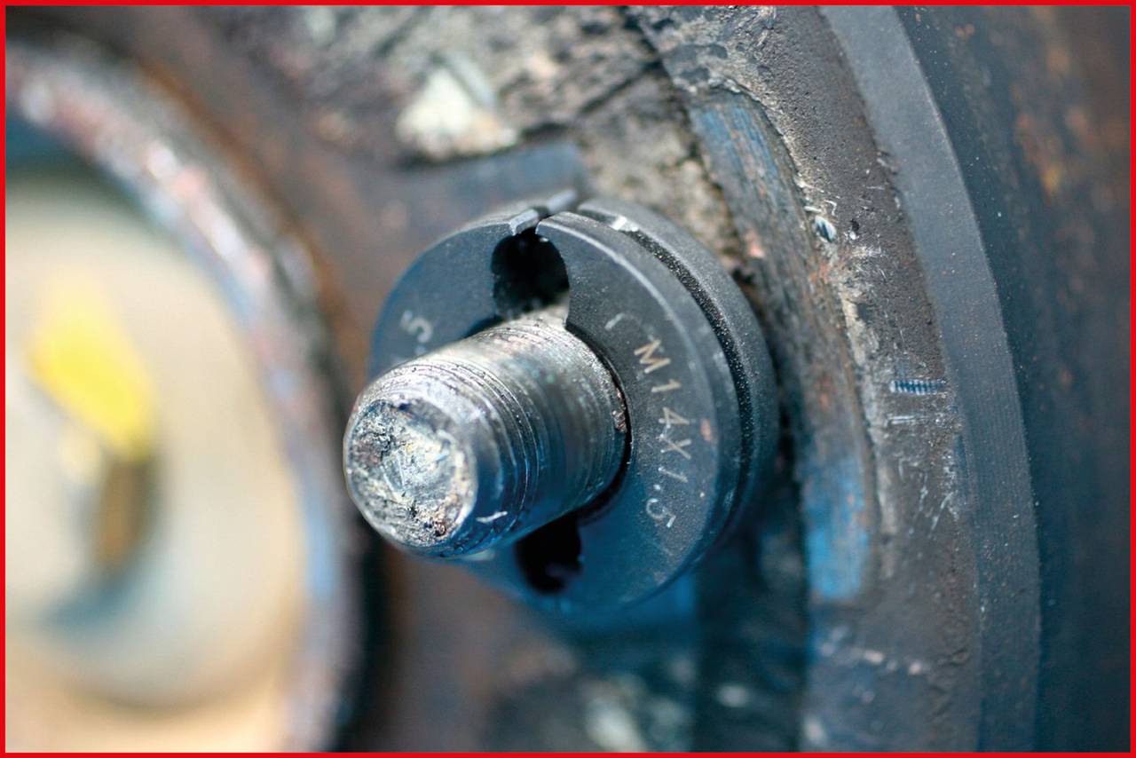 Nahaufnahme eines rostigen Bolzens mit sichtbarem Gewinde, der in eine Metalloberfläche eingeschraubt ist.