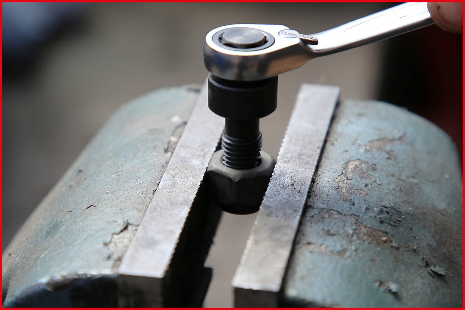 Eine Ratsche zieht eine Schraube in einem Schraubstock fest. Hauptfokus auf dem Werkzeug und Schraubbefestigung.