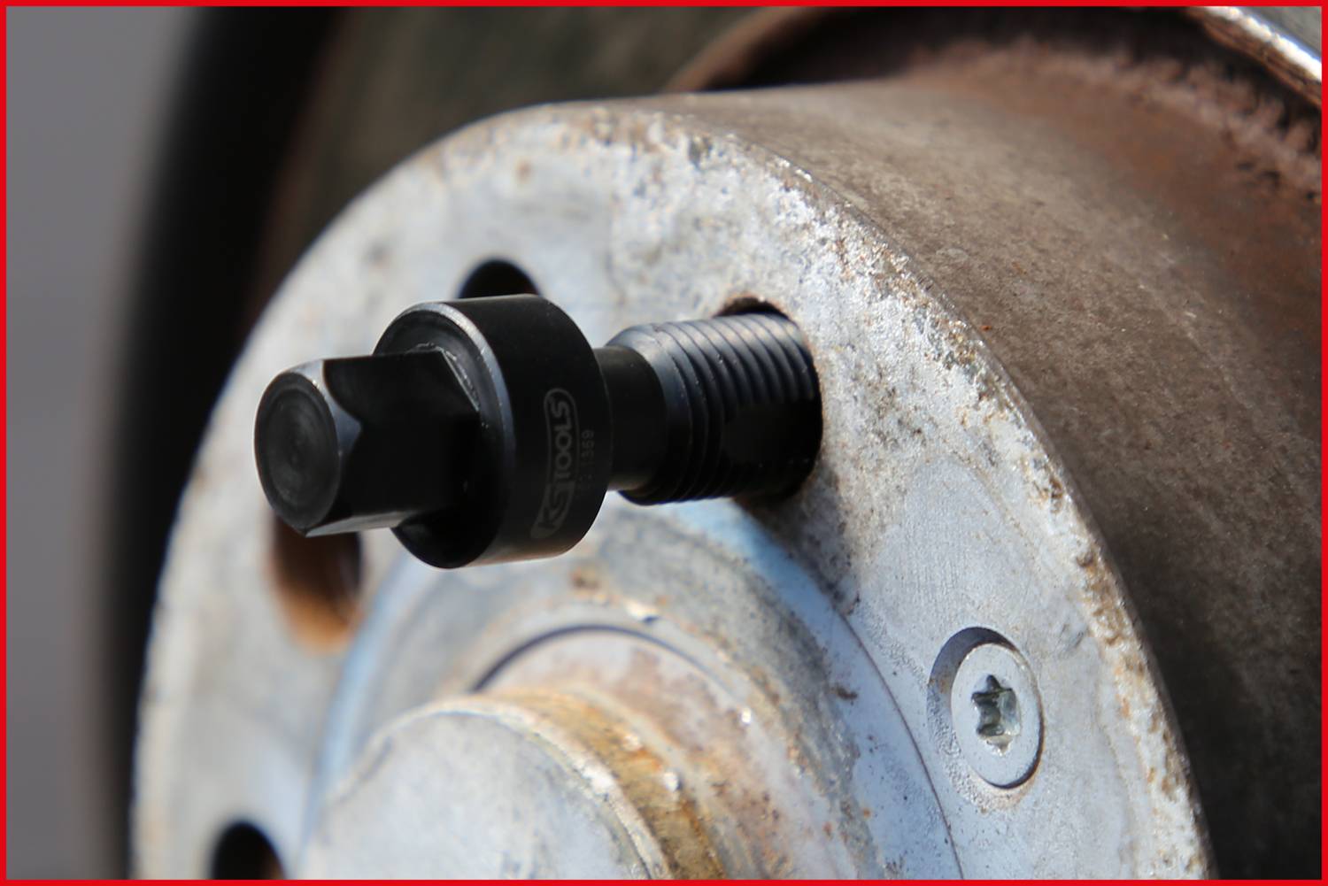 Werkzeug zur Entfernung eines Radlagers, im Nahbereich auf einer rostigen Radnabe montiert. Fokus auf Schraubmechanismus.