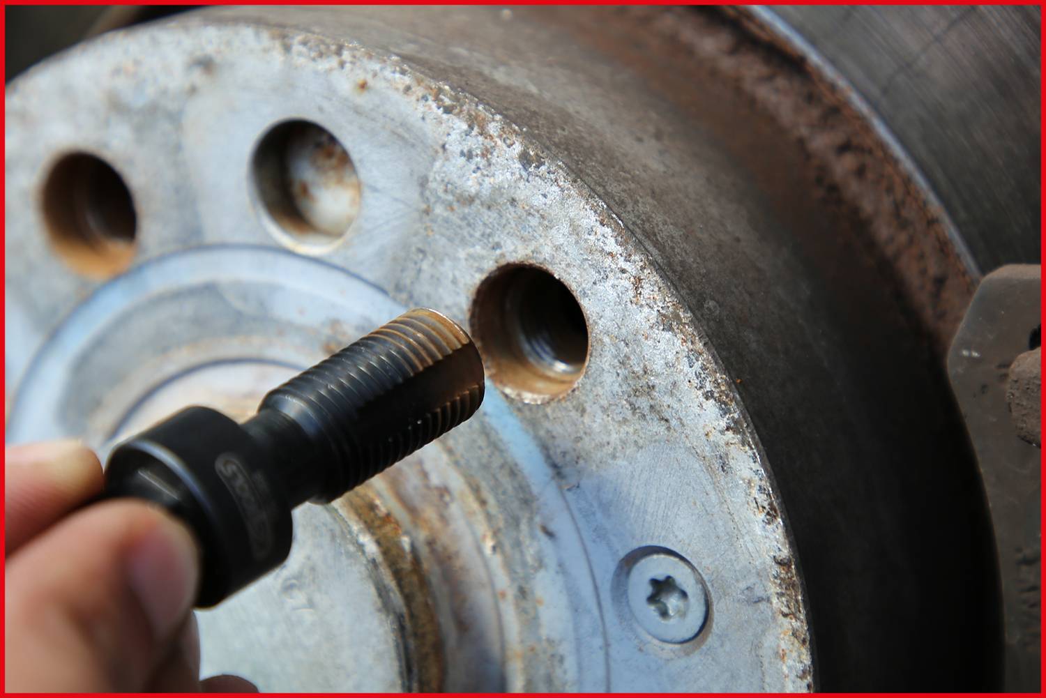 Nahaufnahme eines Bremssystems: Eine Hand hält ein Werkzeug neben einem belüfteten Bremsscheibenrotor, der Anzeichen von Rost aufweist.