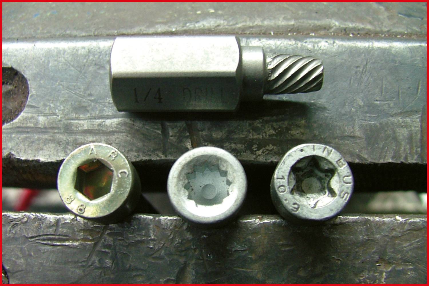 Drei Schraubenköpfe und ein Metallbohrer liegen auf einem Schraubstock. Die Schrauben zeigen verschiedene Innensechskantausführungen.