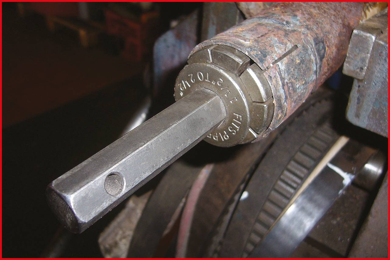Nahaufnahme eines Spanns, der auf einem Metallwerkbank befestigt ist. Rechts im Hintergrund ist ein Teil eines Zahnrads sichtbar.