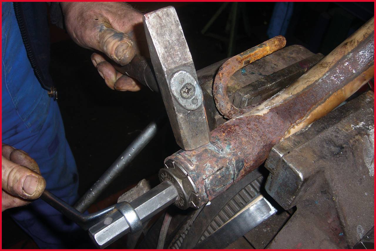 Eine Person repariert ein verrostetes Radlager mit einem Hammer als Werkzeug.