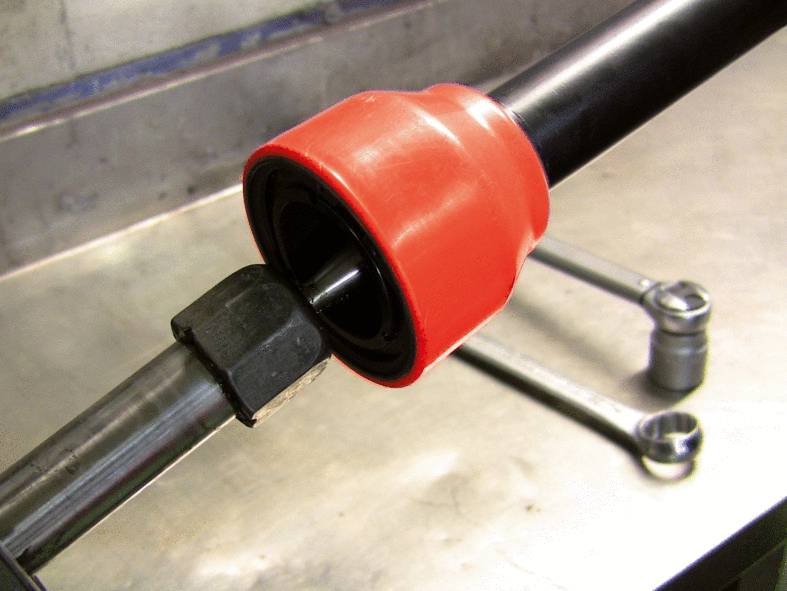 Nahaufnahme eines schwarzen Metallrohrs mit roter Kunststoffummantelung, das in einer maschinellen Vorrichtung befestigt ist, im Hintergrund Werkzeuge.