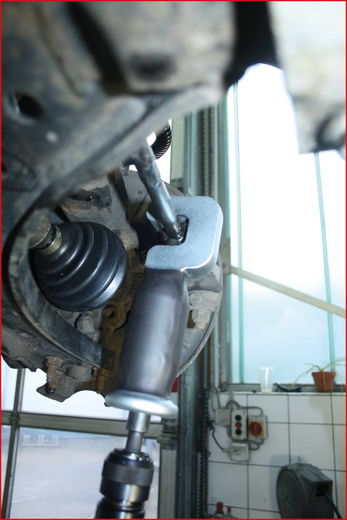 Mechanikerwerkzeug bei der Arbeit an einem Fahrzeugrad. Ein Abzieher entfernt einen Kugelgelenkbolzen vom Fahrwerk.