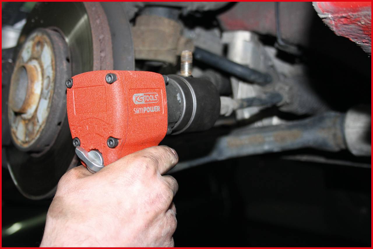 Nahaufnahme einer Hand, die einen roten Druckluftschrauber am Rad eines Autos benutzt. Der Schrauber löst eine Schraube.