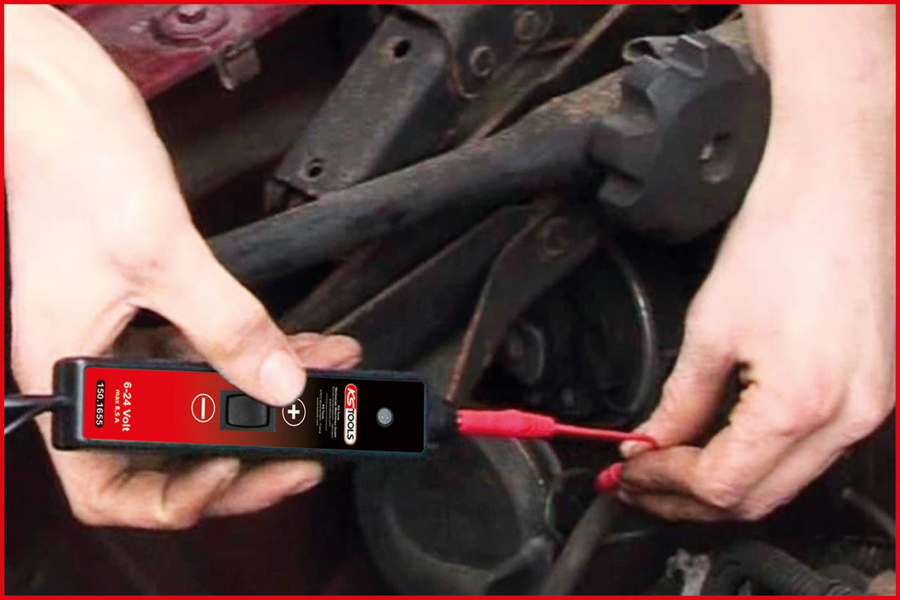 Person testet Autobatterie mit einem Prüfgerät. Rotes Kabel wird an Klemme angeschlossen. Fokus auf Hände und Werkzeug.