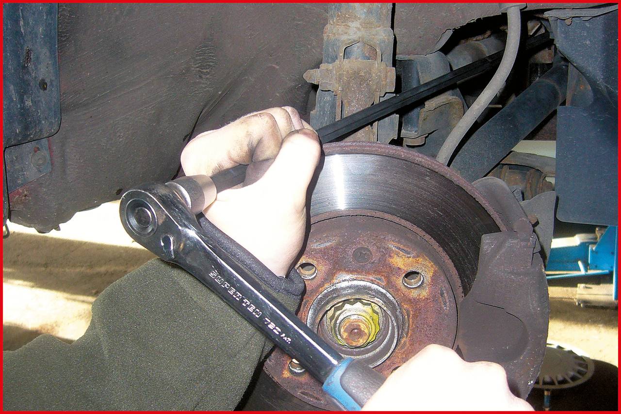 Person repariert ein Auto, verwendet einen Schraubenschlüssel, um die Bremsscheibe am Fahrzeug zu lösen. Automechanische Arbeit.