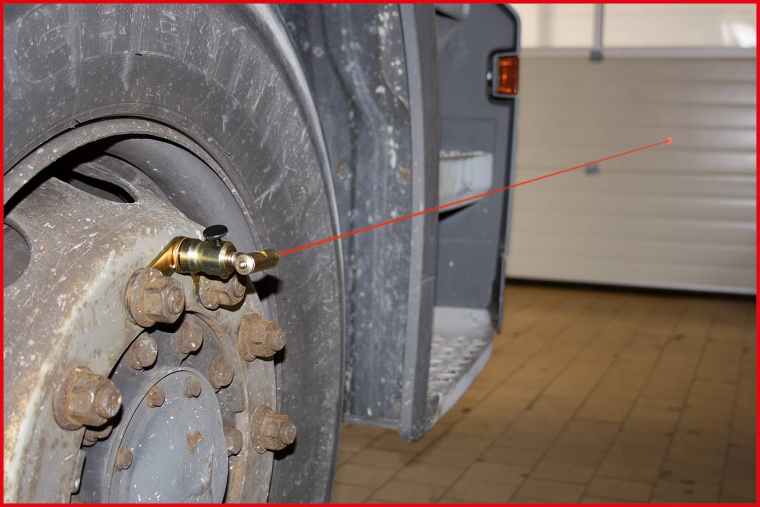 Ein Lkw-Rad mit befestigtem Ventil und Laserentfernungsmesser, der auf ein entferntes Ziel gerichtet ist, in einer Werkstattumgebung.