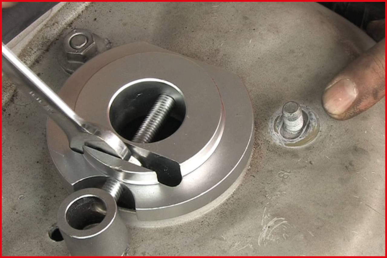 Eine Hand hält einen Schraubenschlüssel, der an einer großen silbernen Mutter auf einer Metallplatte befestigt ist.