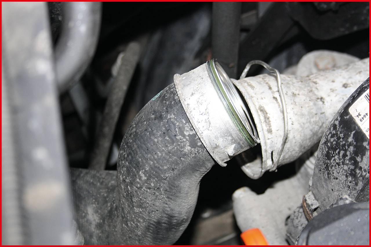 Nahaufnahme eines beschädigten Kühlerschlauchs in einem Motorraum. Der Schlauch ist an einer Schelle lose und leicht verrutscht.