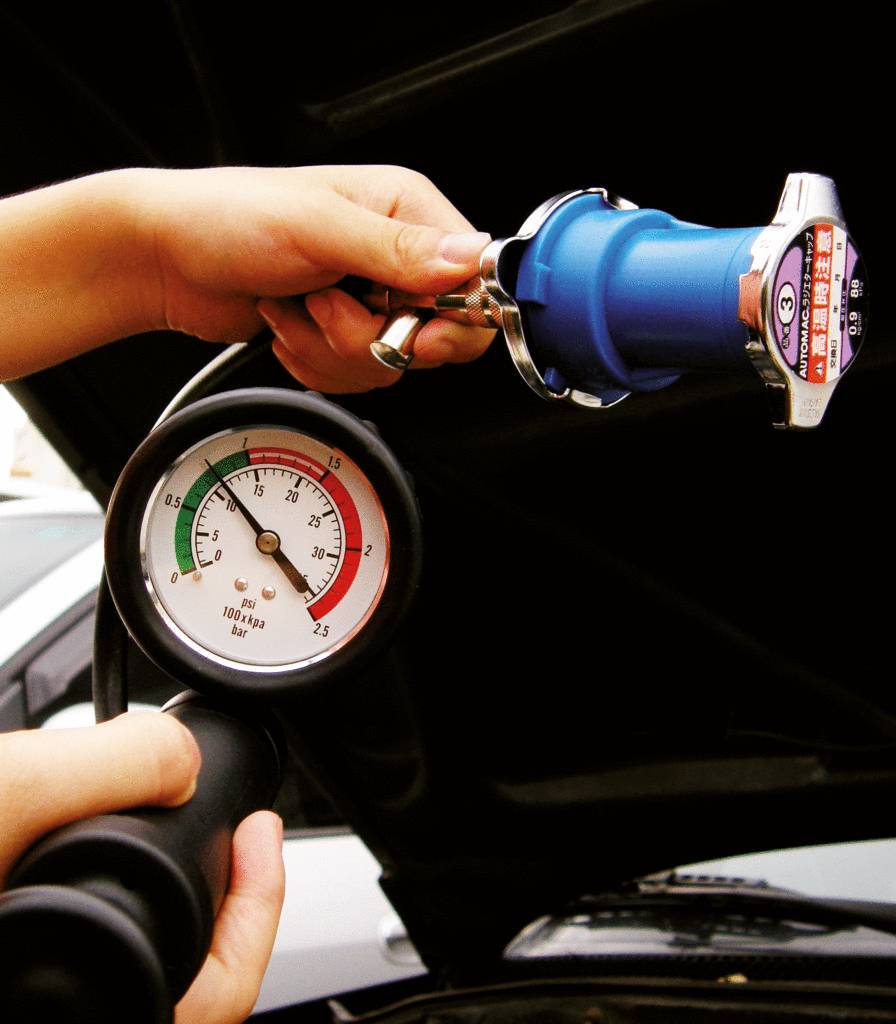 Eine Person hält ein Manometer und ein Kühlertester, um den Druck in einem Autokühlsystem zu überprüfen.