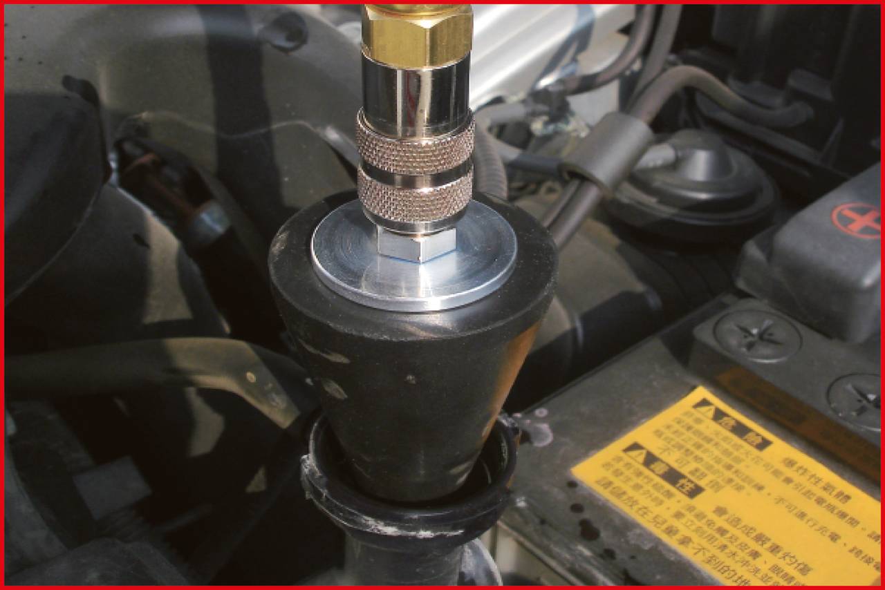 Ein Metallanschluss ist oben an einem schwarzen Gummi- oder Kunststoffteil montiert, umgeben von Autofahrzeugmechanik.