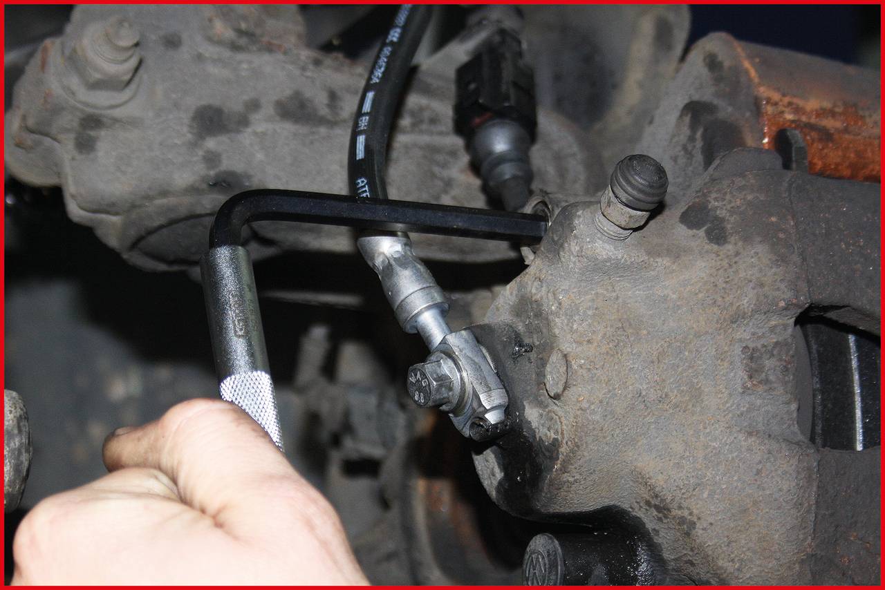 Nahaufnahme eines Automechanikers, der mit einem Inbusschlüssel an einer Bremse arbeitet. Der Fokus liegt auf der Hand und dem Werkzeug.