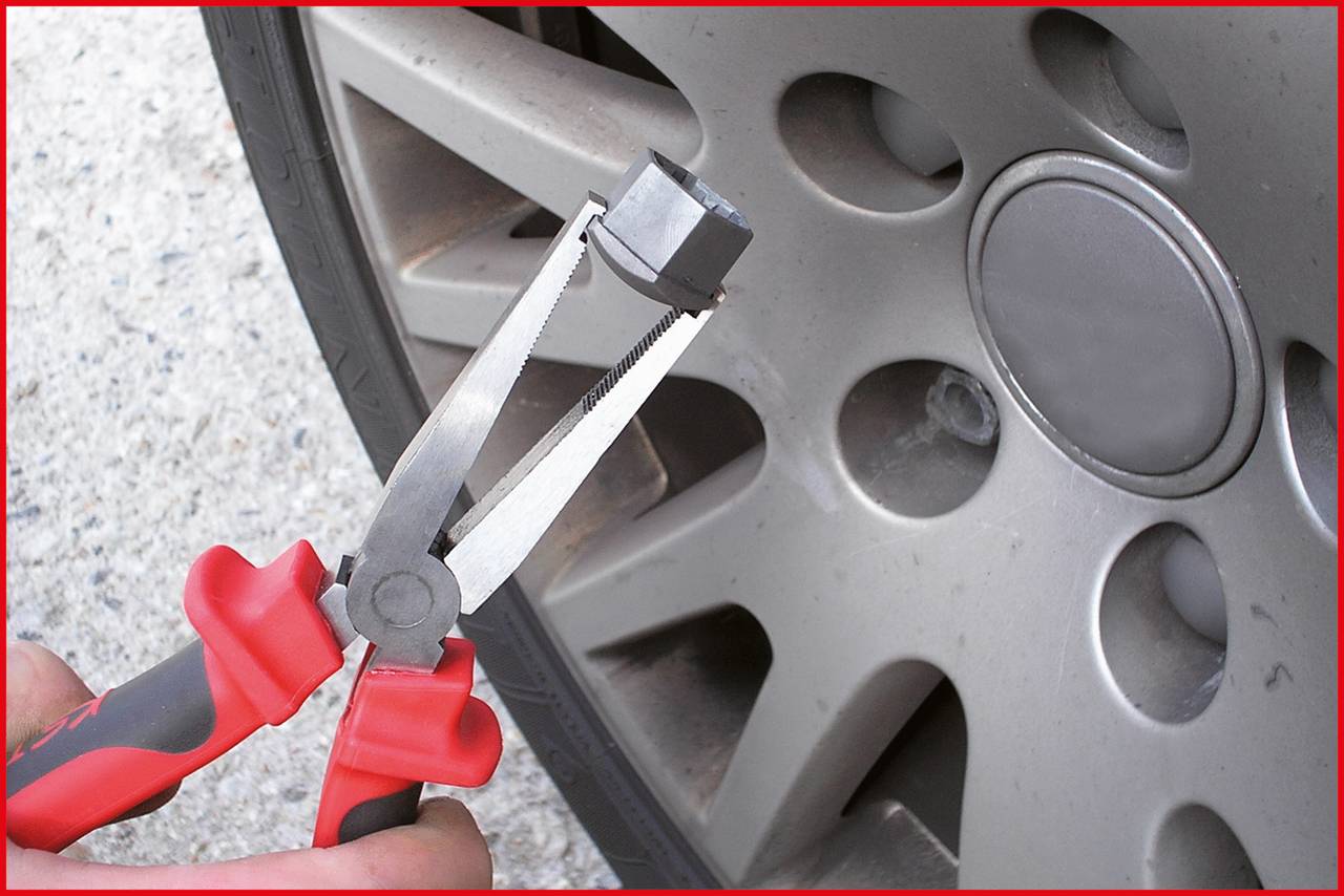 Nahaufnahme einer Zange, die eine Radmutterkappe vor einem Autoreifen hält. Hintergrund zeigt Reifen und Felge.