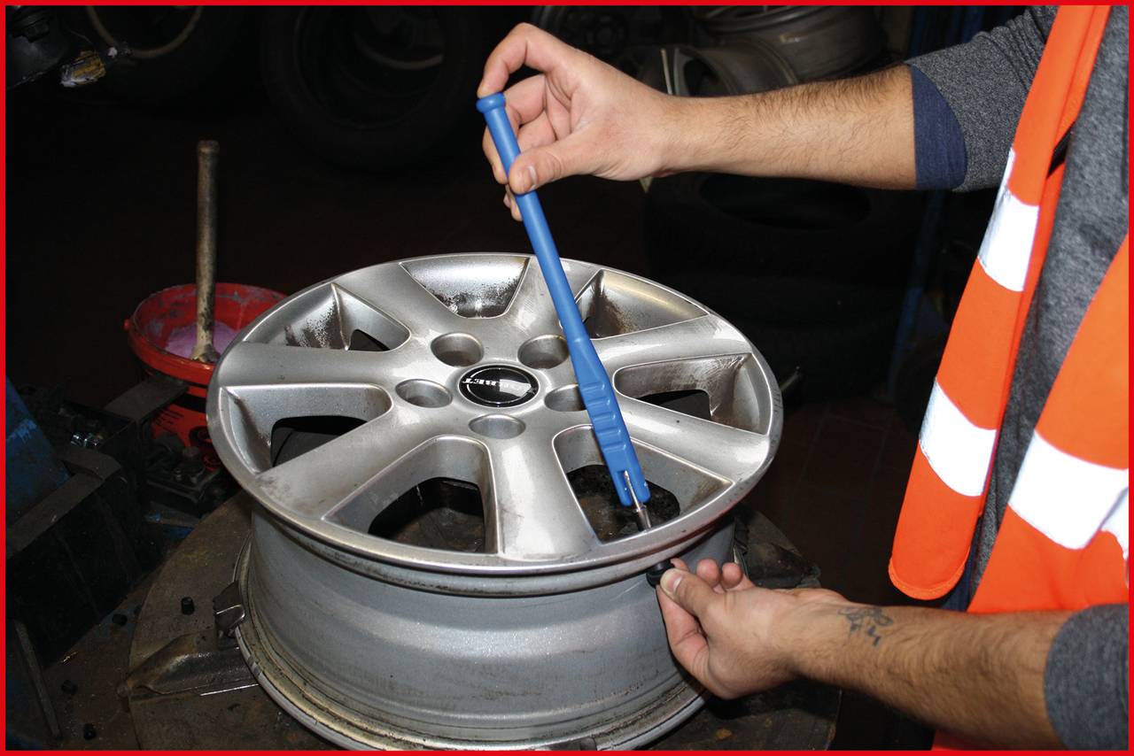 Eine Person überprüft mit einem blauen Werkzeug die Felge eines Autos. Sie trägt eine orange Warnweste.