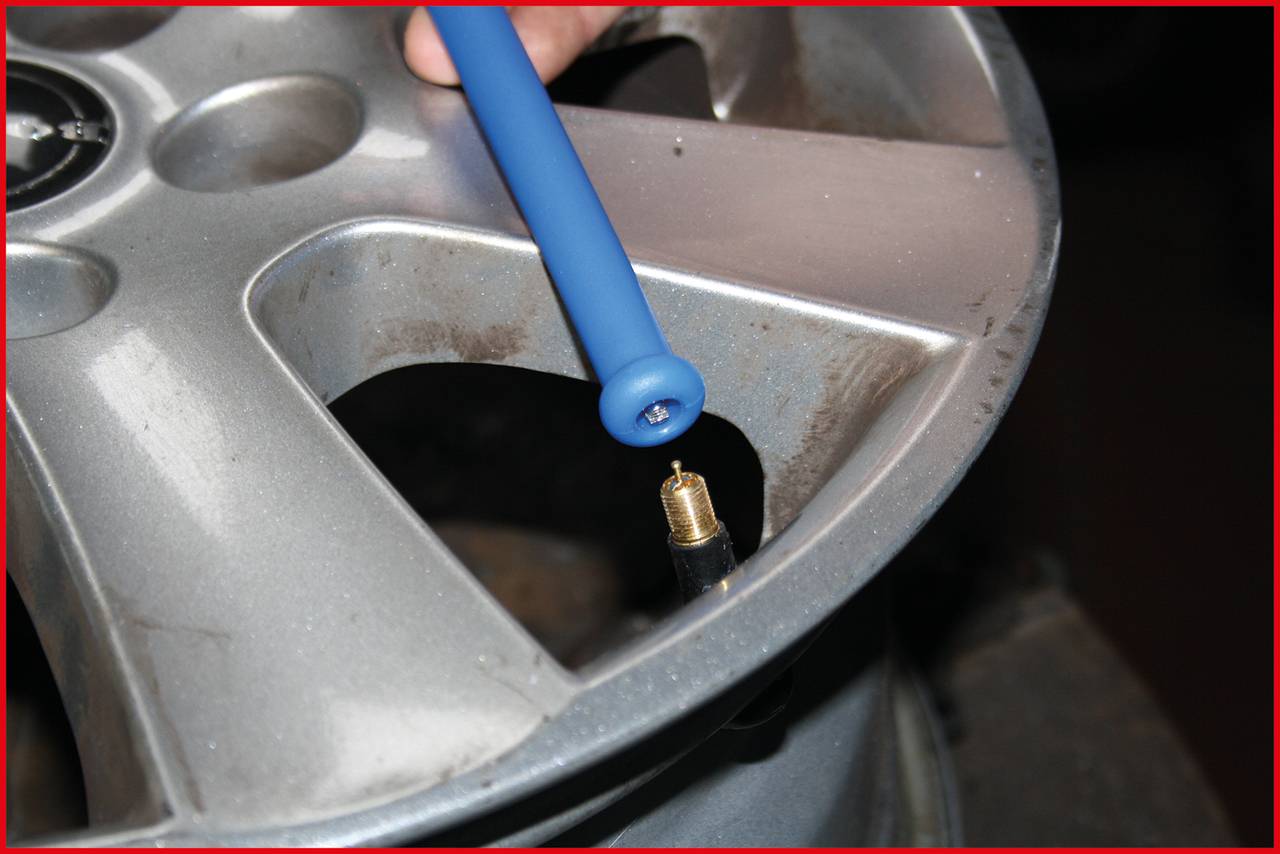 Reifen wird mit einem blauen Werkzeug überprüft. Das Ventil ist sichtbar. Hauptfokus liegt auf der Inspektion des Rades.