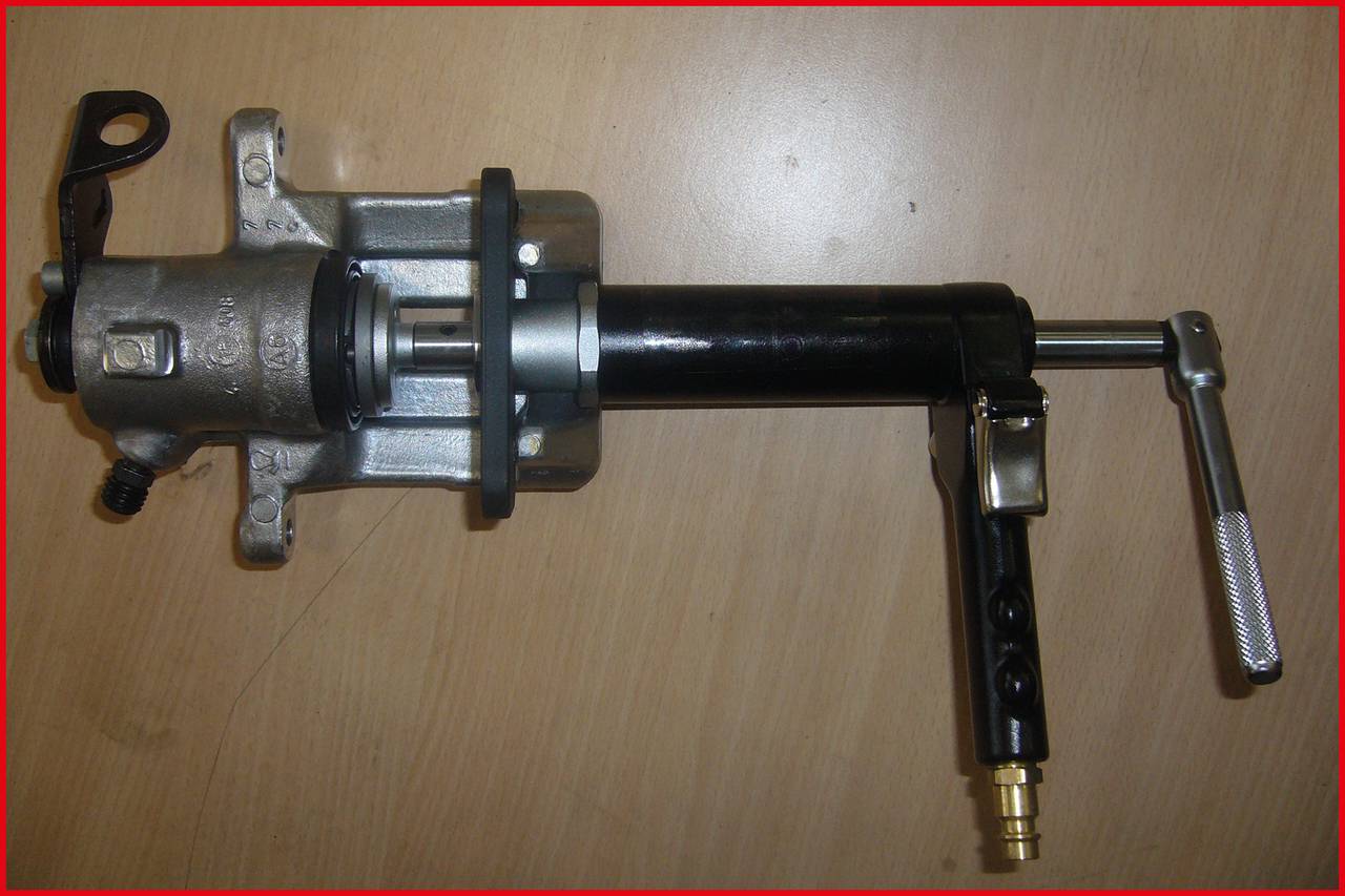 Hydraulische Vorrichtung auf einem Holztisch. Verfügt über einen Griff, Kolben und Hebel, vermutlich für industrielle Anwendungen.