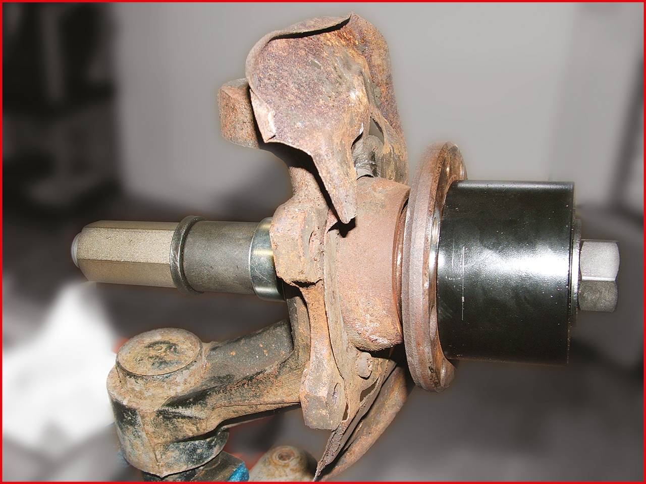 Rostiges Autoteil aus Metall, das eine Achse mit einer Radnabe zeigt, möglicherweise ein altes oder defektes Fahrzeugteil.