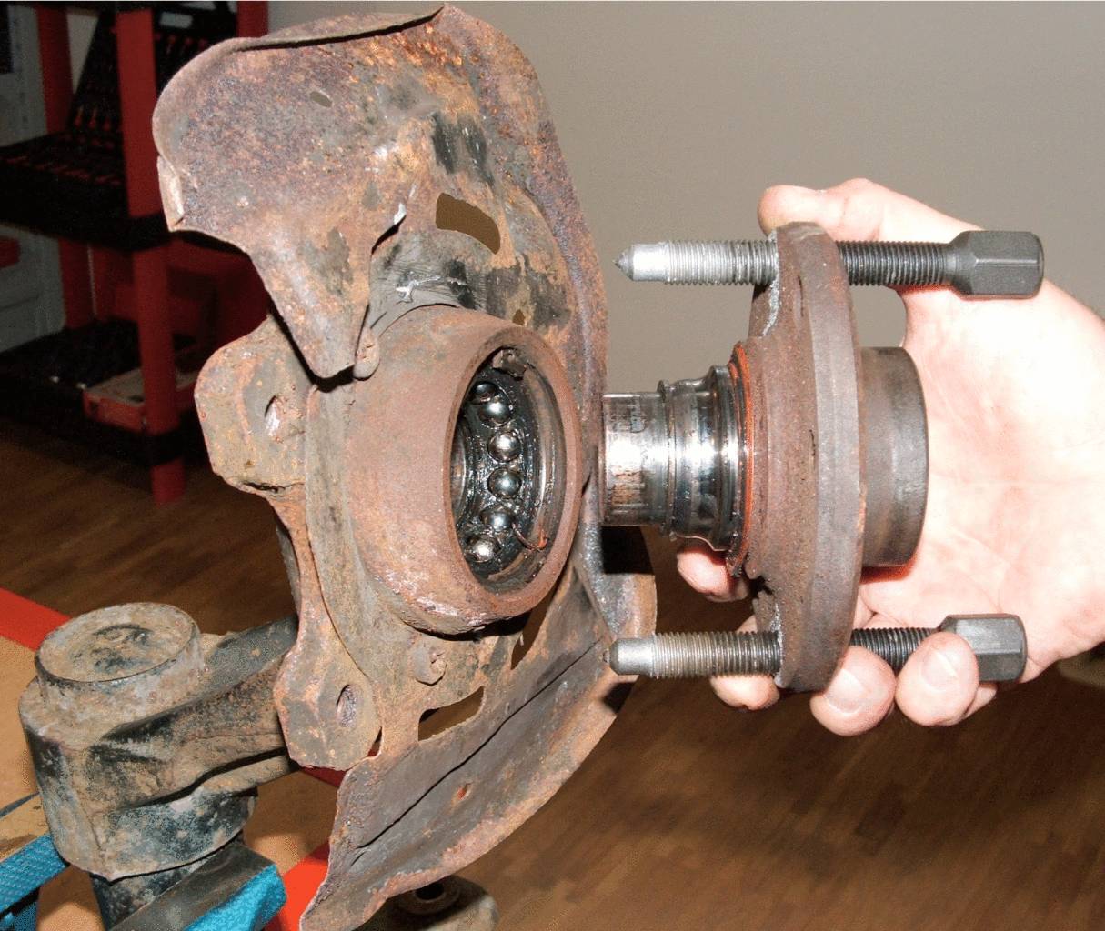 Eine Hand hält ein rostiges Autoteil mit Kugellager, vermutlich ein Radlager. Das Lager scheint abgenutzt und in einem Reparaturkontext.