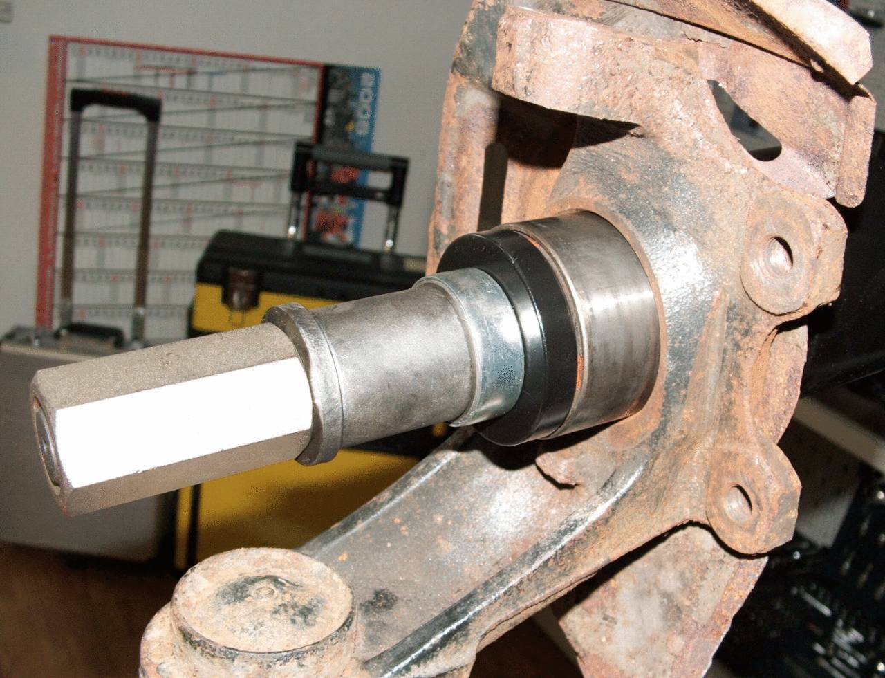 Ein Werkzeug wird benutzt, um ein Lager in einem Metallrahmen zu platzieren. Im Hintergrund ist ein gelber Werkzeugkasten sichtbar.