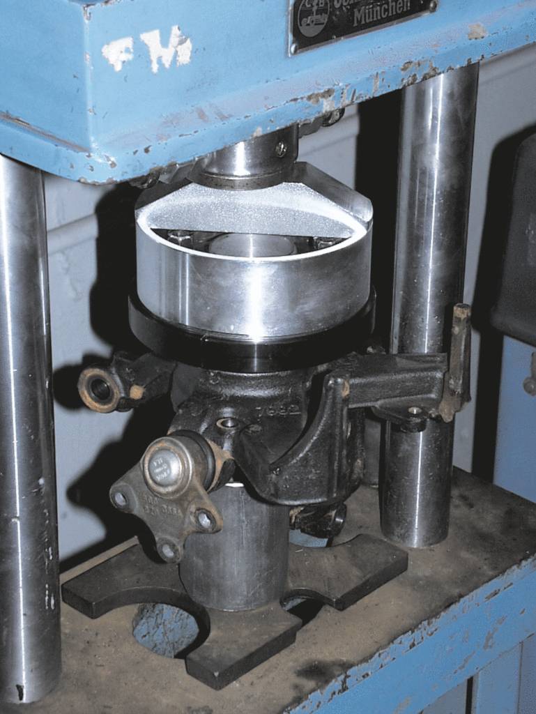 Eine hydraulische Presse in einer Werkstatt, die ein silbernes Metallstück formt.