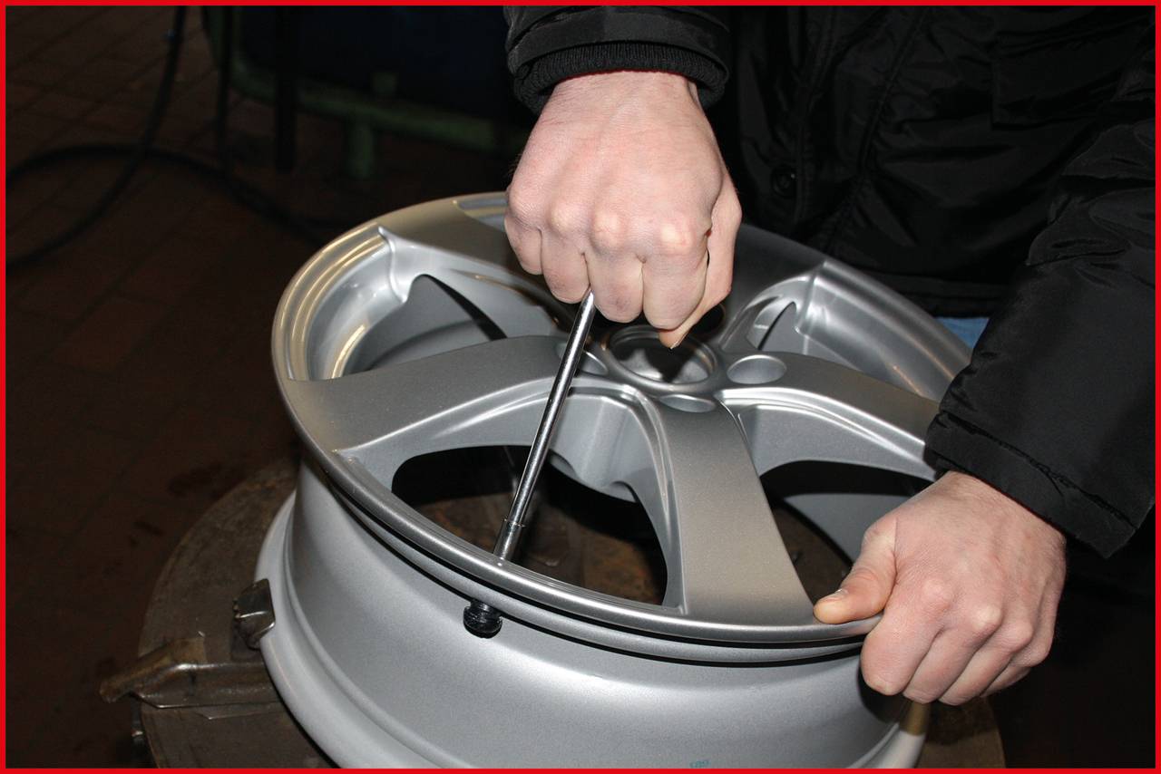 Zwei Hände ziehen mit einem Schraubenschlüssel an der Mutter einer silbernen Autofelge, um sie zu befestigen oder zu lösen.