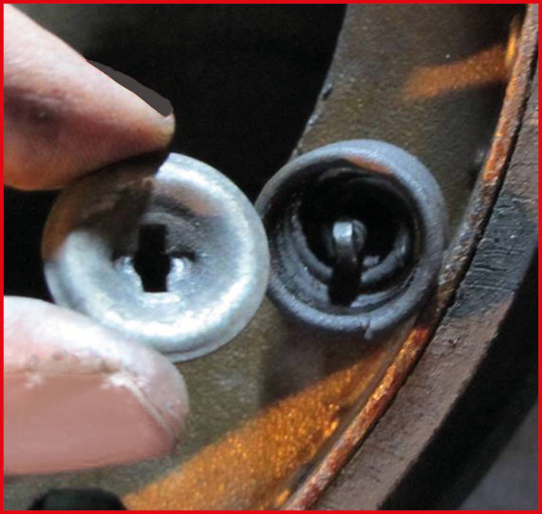 Zwei abgenutzte Schrauben: Eine wird von einer Hand gehalten, die andere ist in einer Metalloberfläche montiert.