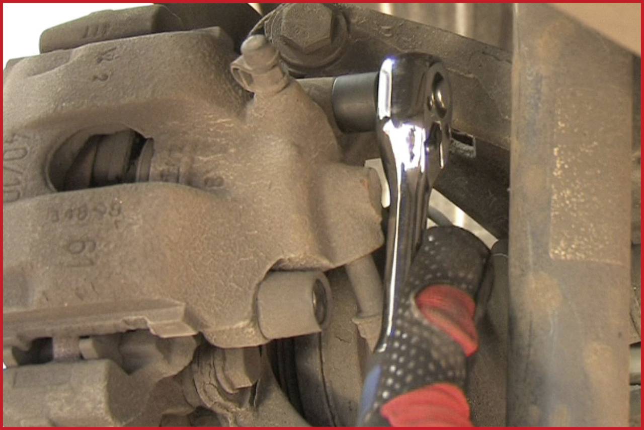 Ein Schraubenschlüssel wird an einer verrosteten Mutter eines Autoteils angesetzt. Ein Mechaniker arbeitet an der Reparatur.