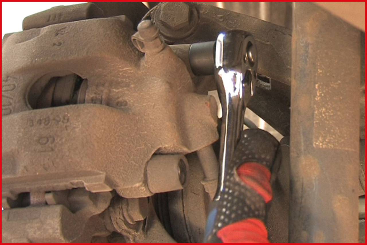 Eine Ratsche wird verwendet, um eine Schraube an einem Bremssattel zu befestigen. Nahaufnahme zeigt mechanische Details der Autoreparatur.