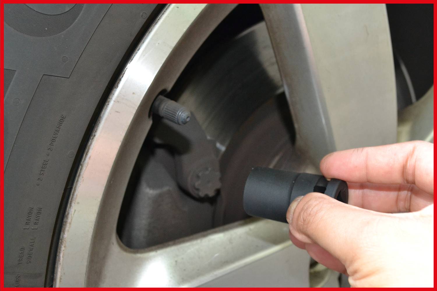 Eine Hand hält ein Magnetventildeckel nahe an den Reifenventilschaft eines Autos, bereit zum Aufsetzen. Das Rad ist teilweise sichtbar.